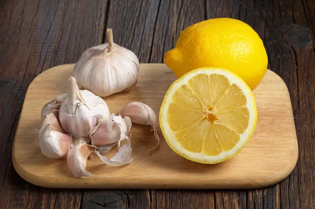 Žlutá citronová polovina s česnekem na dřevěném prknu.