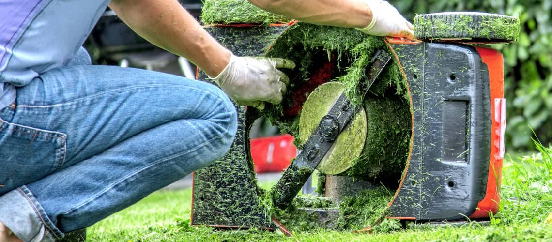 Člověk čistí trávu z podvozku benzínové sekačky