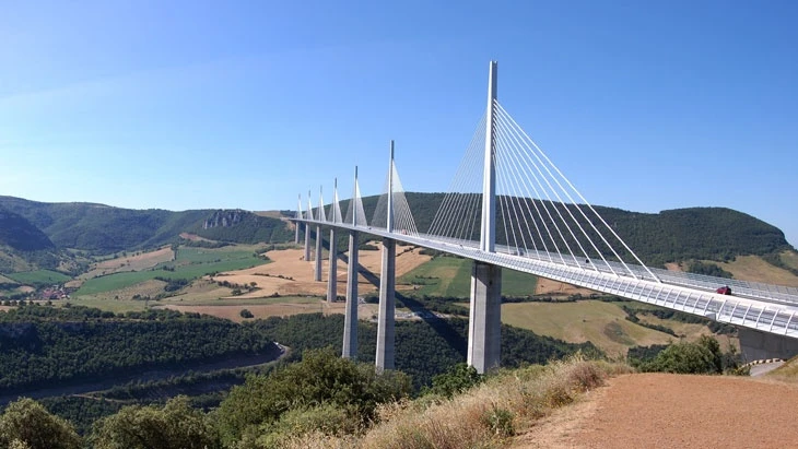 Viadukt Millau přes údolí s kopci na pozadí.