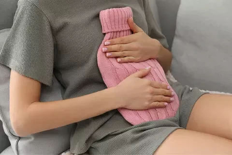 Žena s horkou fľaškou na žaludku při křečích.