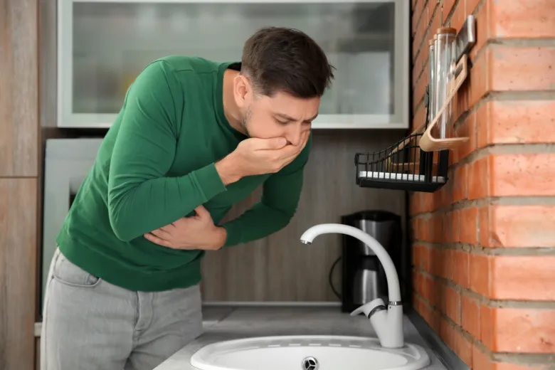 Muž se ohybuje nad umyvadlem kvůli nevolnosti.