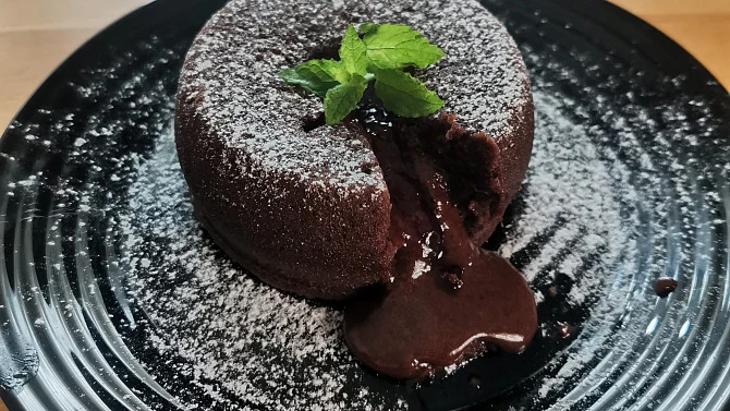 Čokoládový fondant s tekutou čokoládou na černém talíři.