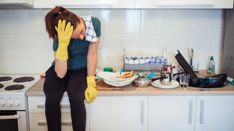 Unavená žena sedí v kuchyni uprostřed nepořádku.