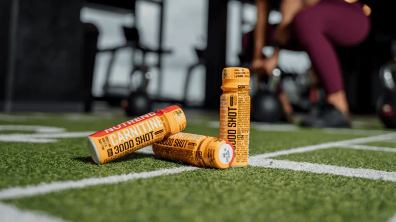 Carnitine supplement bottles on turf with person working out