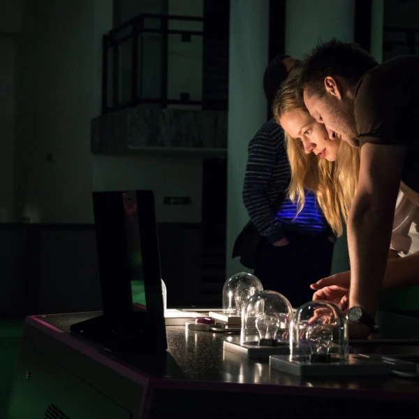 Lidé zkoumají elektronické komponenty na stole v tmavé místnosti.