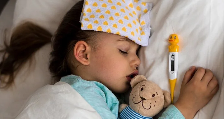 Malá nemocná dívka spí s teploměrem na lůžku.