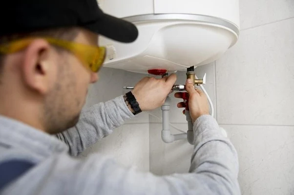 Technik opravuje bojler s viditelnými vodovodními přípojkami.