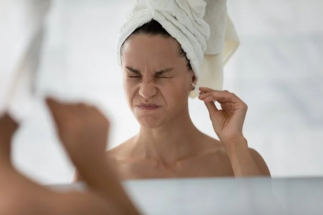 Žena se dívá do zrcadla a prohlíží si ucho.