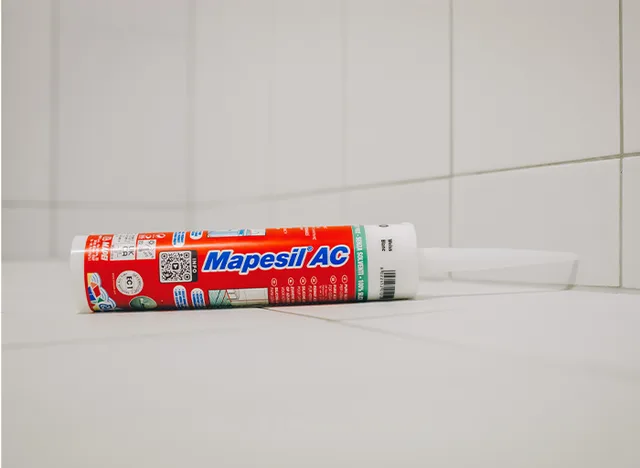Tubka sanitárního silikonu Mapesil AC na dlažbě v koupelně.