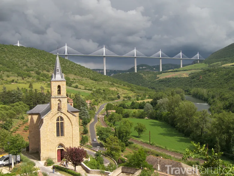 Viadukt Millau v údolí s kostelem na popředí pod mraky.