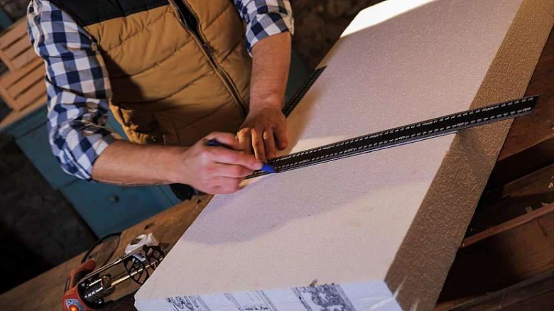 Muž řezá bílý styrofoam dlouhým nožem podél pravítka.