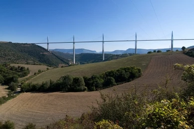 Viadukt Millau přes údolí s kopci pod modrou oblohou.
