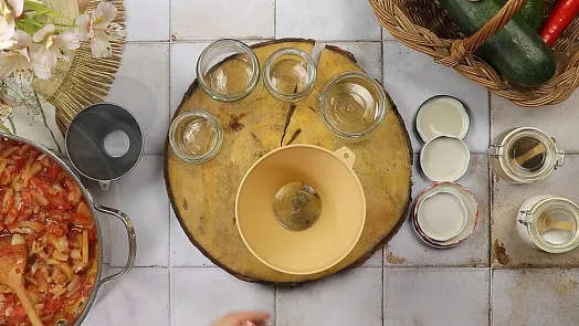 Nakládání rajčat s ingrediencemi a nádobami na kuchyňské desce.