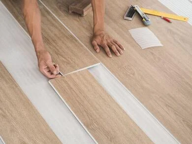 Muž leží na podlaze a ukládá dlaždice z vinylového potahového materiálu.