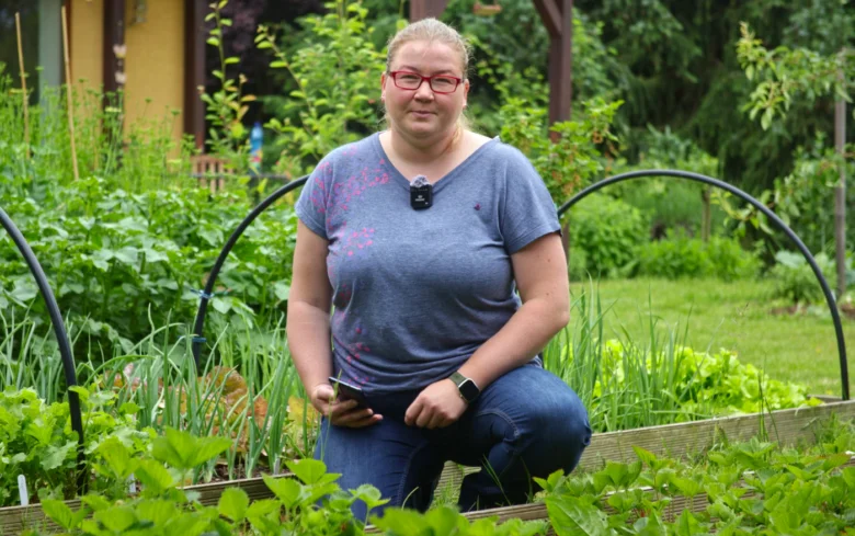 Žena v zahradě s zeleninou na pozadí rostlin.