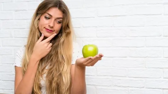 Mladá žena drží zelené jablko v ruce.