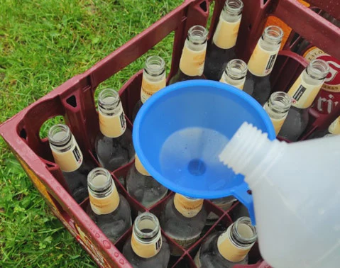 Nalévání moštu do lahví pomocí modrého funku na trávníku.