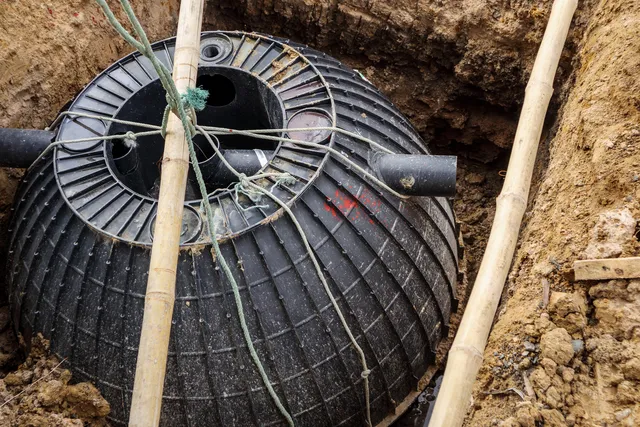 Černý septik v jámě během instalace s hadicemi a podpěrami.