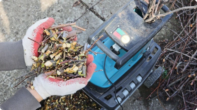 Ruce drží dřevěné štěpky vedle elektrického štěpkovače
