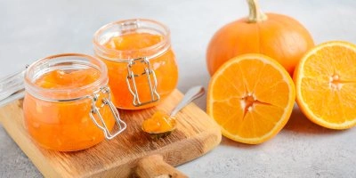 Dýňová marmeláda s pomerančem v sklenicích vedle čerstvých citrusů.
