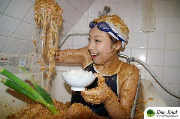 Žena v koupeli s natto na těle drží misku rýže.
