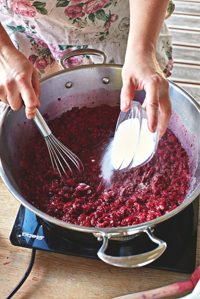 Přidávání cukru do vařících švestek při výrobě domácí marmelády.