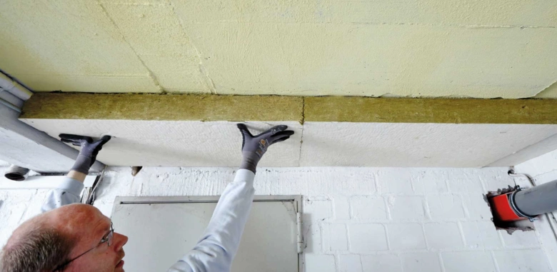 Muž instaluje izolační materiál na strop v nehotové místnosti.