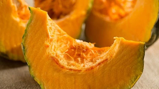Čerstvé kousky dýně s oranžovou dužinou a zelenou slupkou.