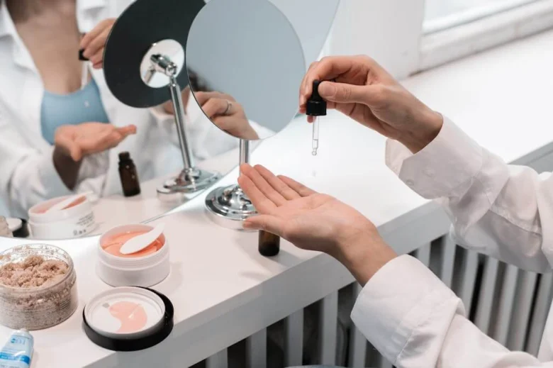 Žena v bílém plášti aplikuje kapku kosmetického produktu do ruky