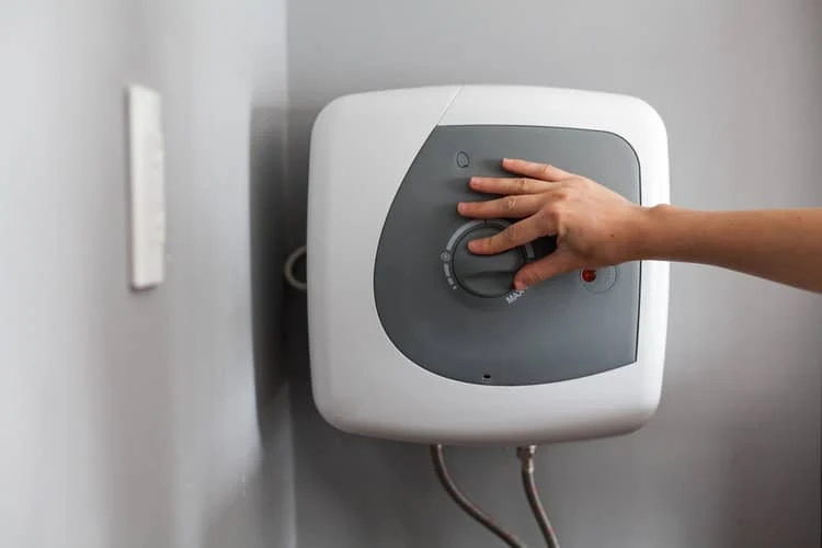 Ruka nastavuje teplotu na elektrickém bojleru.