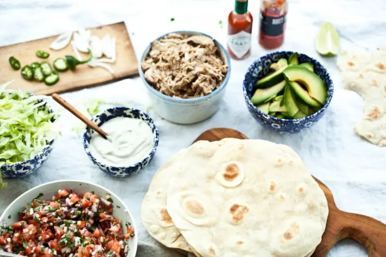 Suroviny na tacos: tortilly s masem, avokádem a omáčkami.
