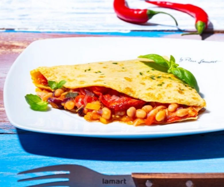 Tortilla plněná fazolemi, zeleninou a bazalkou na bílém talíři.