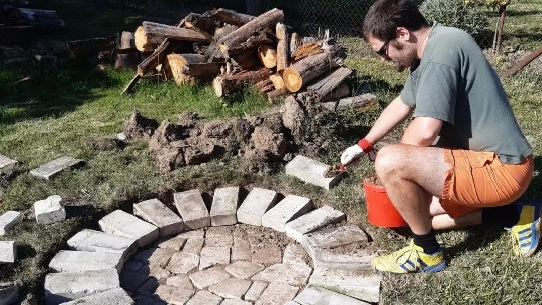 Muž kladne cihly do kruhového okraje terasy v zahradě.